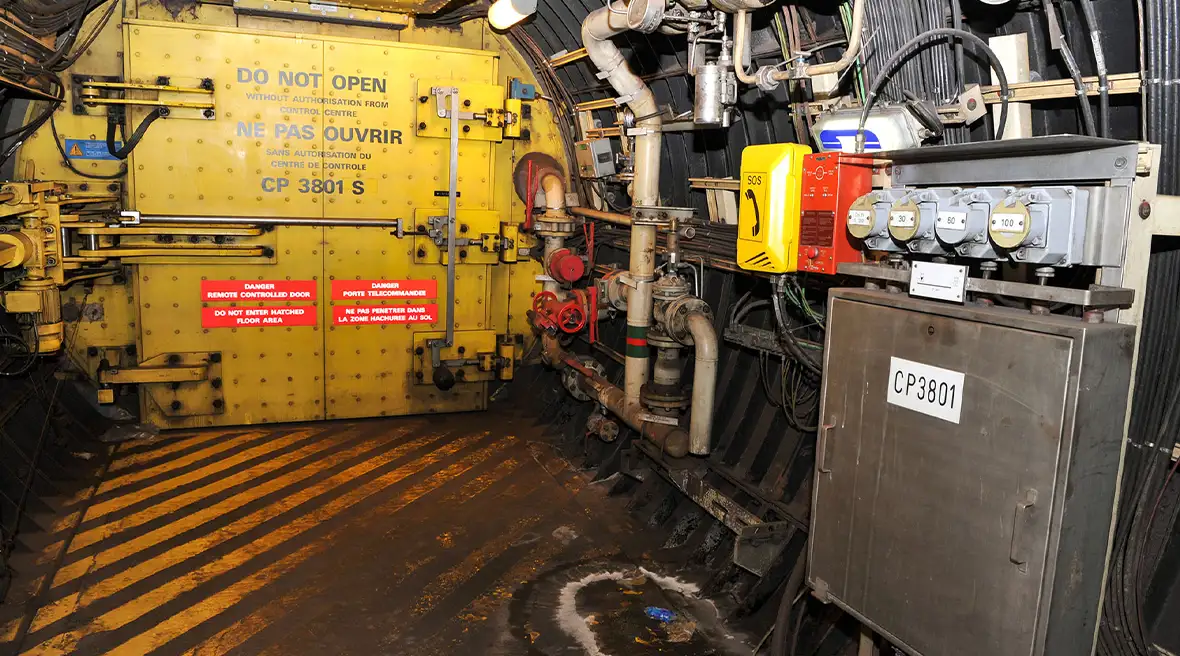 Large metal door on yellow and black striped flooring stained from use and metal fuse boxes and controls on the wall