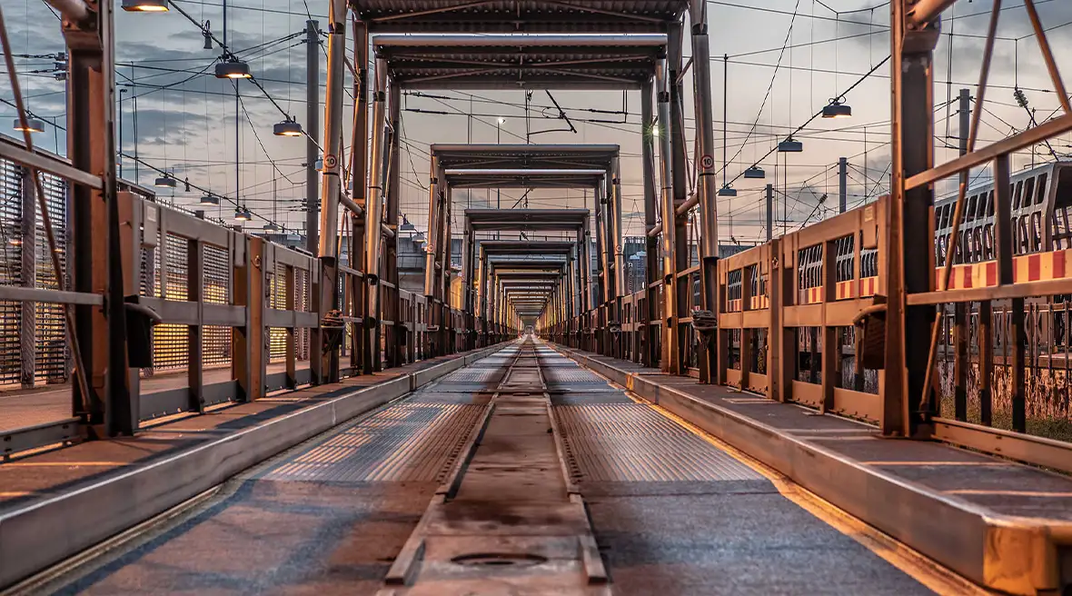 Sunset on a long stretch of shuttle track made from metal with lights strung along each side