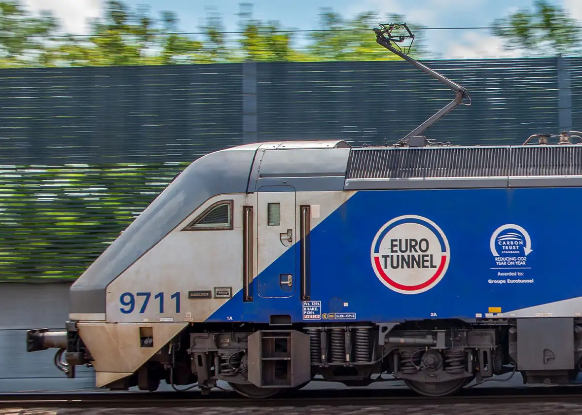 Front of a blue and white Eurotunnel Le Shuttle train with 9711 on the front with blue skies and green trees above