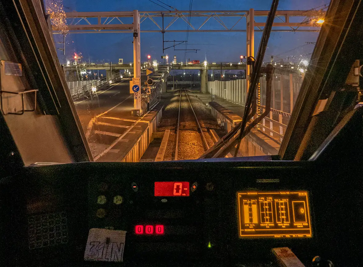 A view of the Eurotunnel track ahead of a driver from inside the cabin with controls lit up and a blue night sky with rain on the window