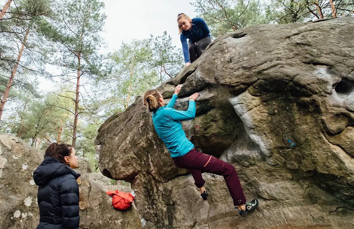 Three women helping each other to navigate a large boulder