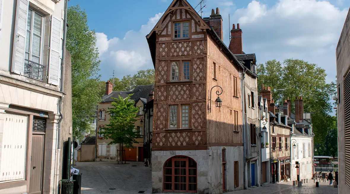 Historic 4-storey medieval house on a cobbled street corner, the street slopes down with sunlight evocatively hitting the old buildings