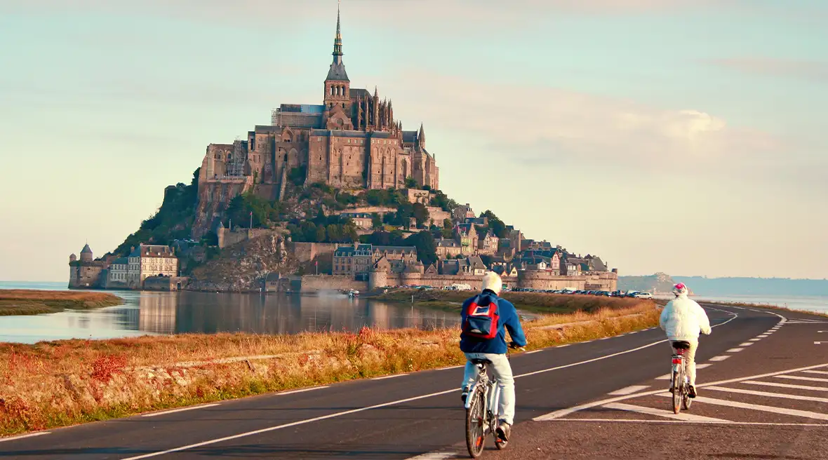 a couple cycling towards a beautiful city on a hill surrounded by water with blue clear skies