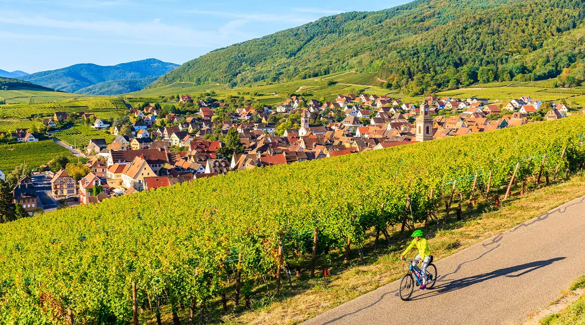 Young woman cycling among vineyards on road above a pretty French village on a wine route in France
