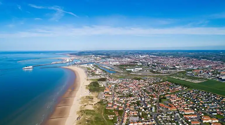 aerial view of a port with blue water sandy beach and lots of buildings under a blue sky
