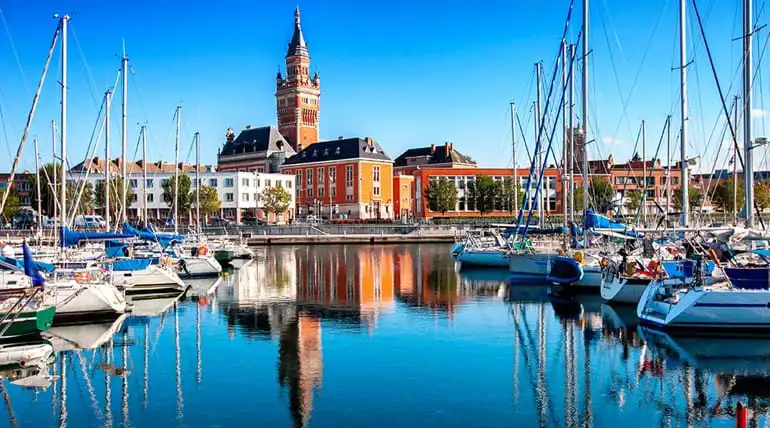 harbour full of boats with historic red brick building in distance and reflected in water