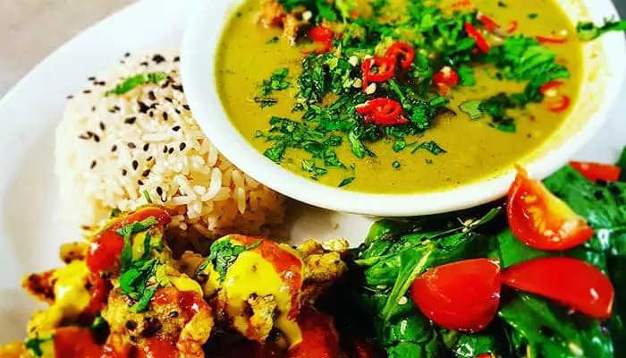 Een bord goudgele hummus met linzenpuree, wortelen, bieten, bloemen en groene saus