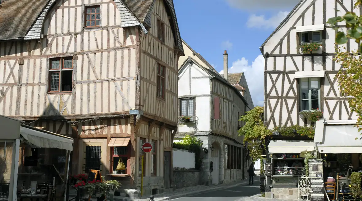 large wood timbered houses on a small cobbled street with a shop and market stall in the foreground