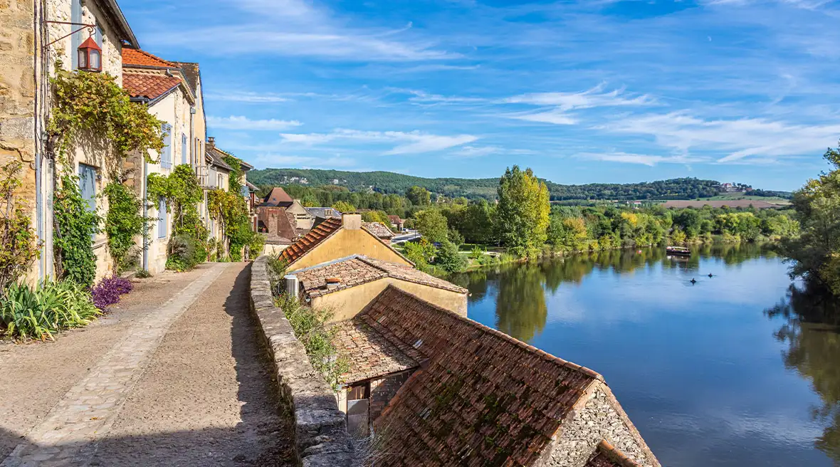 Pretty riverside houses and cobbled embankment by a peaceful bend in a river on a summer’s day