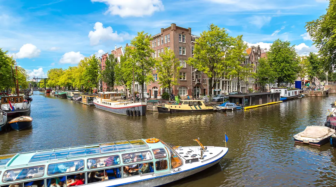 Boat on the canal with brown building and trees in the background