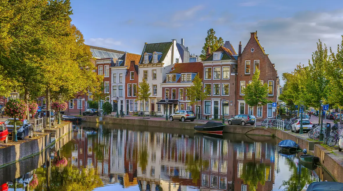Trees and multicolored buildings lining a curved river with their reflection mirrored in the water