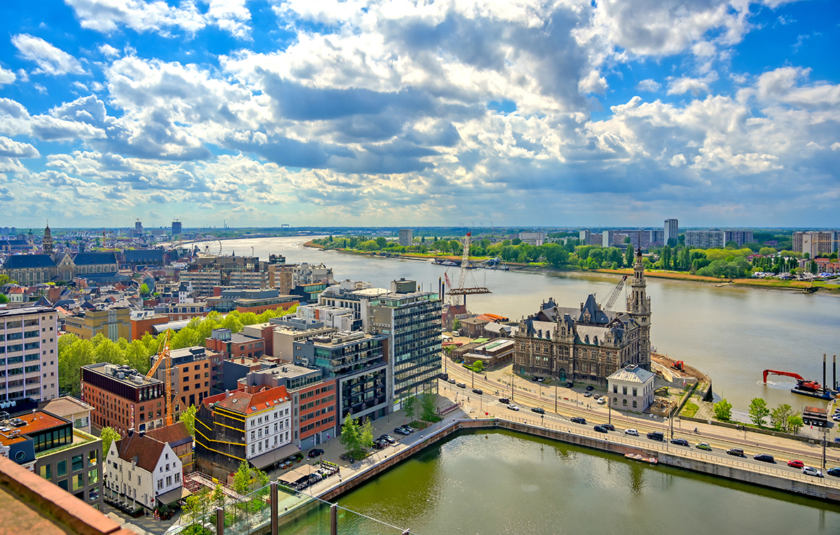 aerial view of the port and docks in Antwerp Belgium with rows of buildings lining the water and a blue sky filled with clouds above