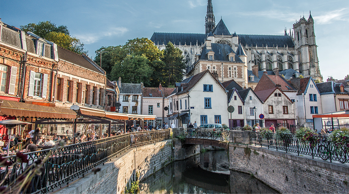 A cathedral overlooks lower level buildings and an attractive bridge over a river in an old part of a city