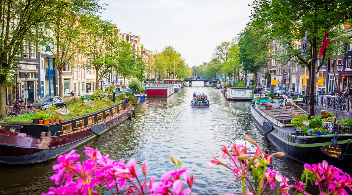 boats on a river with trees, buildings, and flowers lining the banks