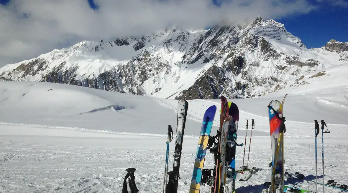 Multicoloured skiing poles and Skis standing in the snow in front of snow covered mountains that are as high as the clouds