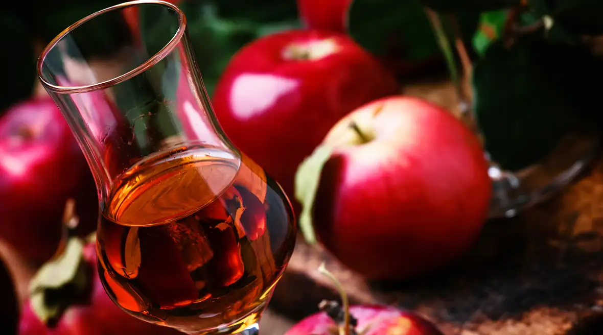 A glass of a dark alcoholic spirit with apples around it