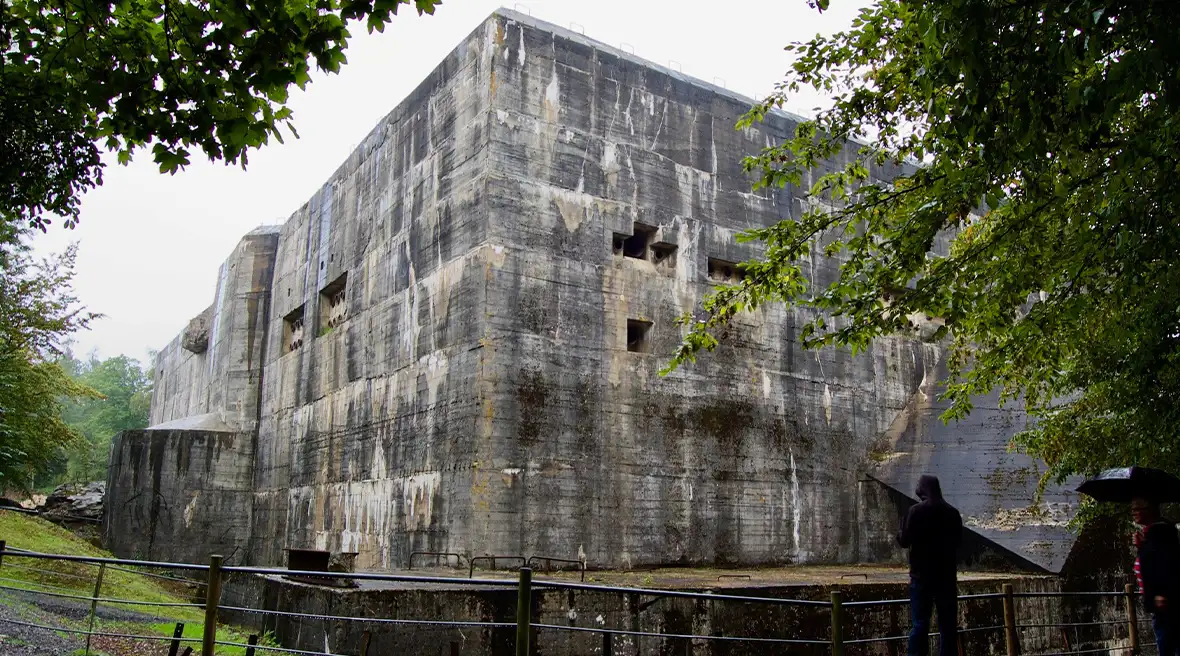 An ugly featureless and windowless military building in a forest clearing. A person stands in front of it.