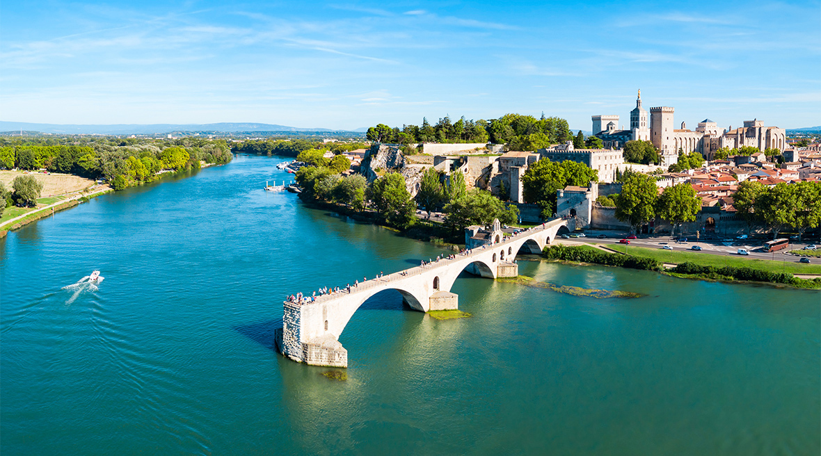 An old stone bridge that only goes part way across a wide river, from a historic town with a castle and fortifications