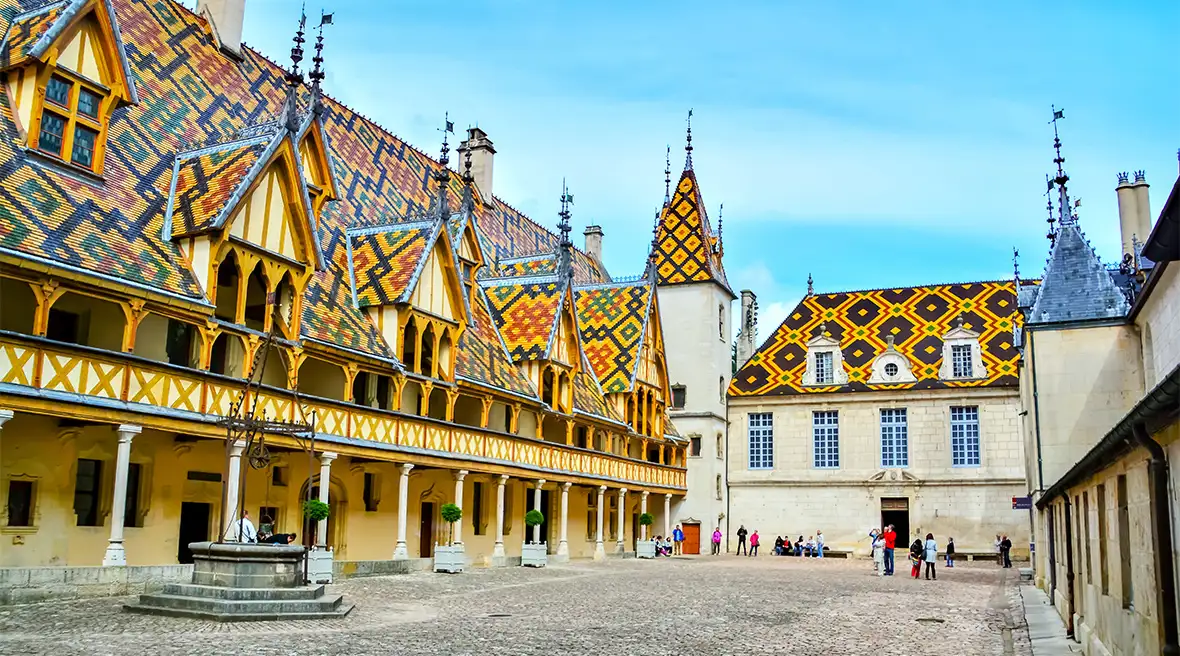 A cobbled courtyard of very colourfully tiled long building, with pillars and gables
