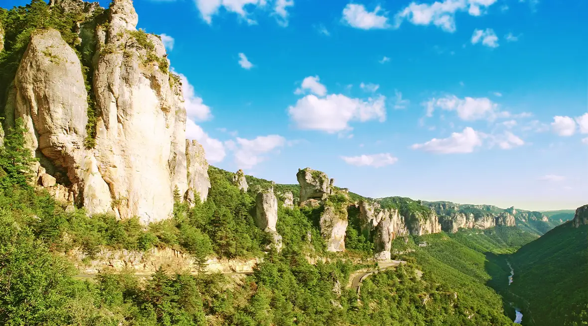 Rock outcrops rise above a wooded gorge with a river at the bottom of the valley