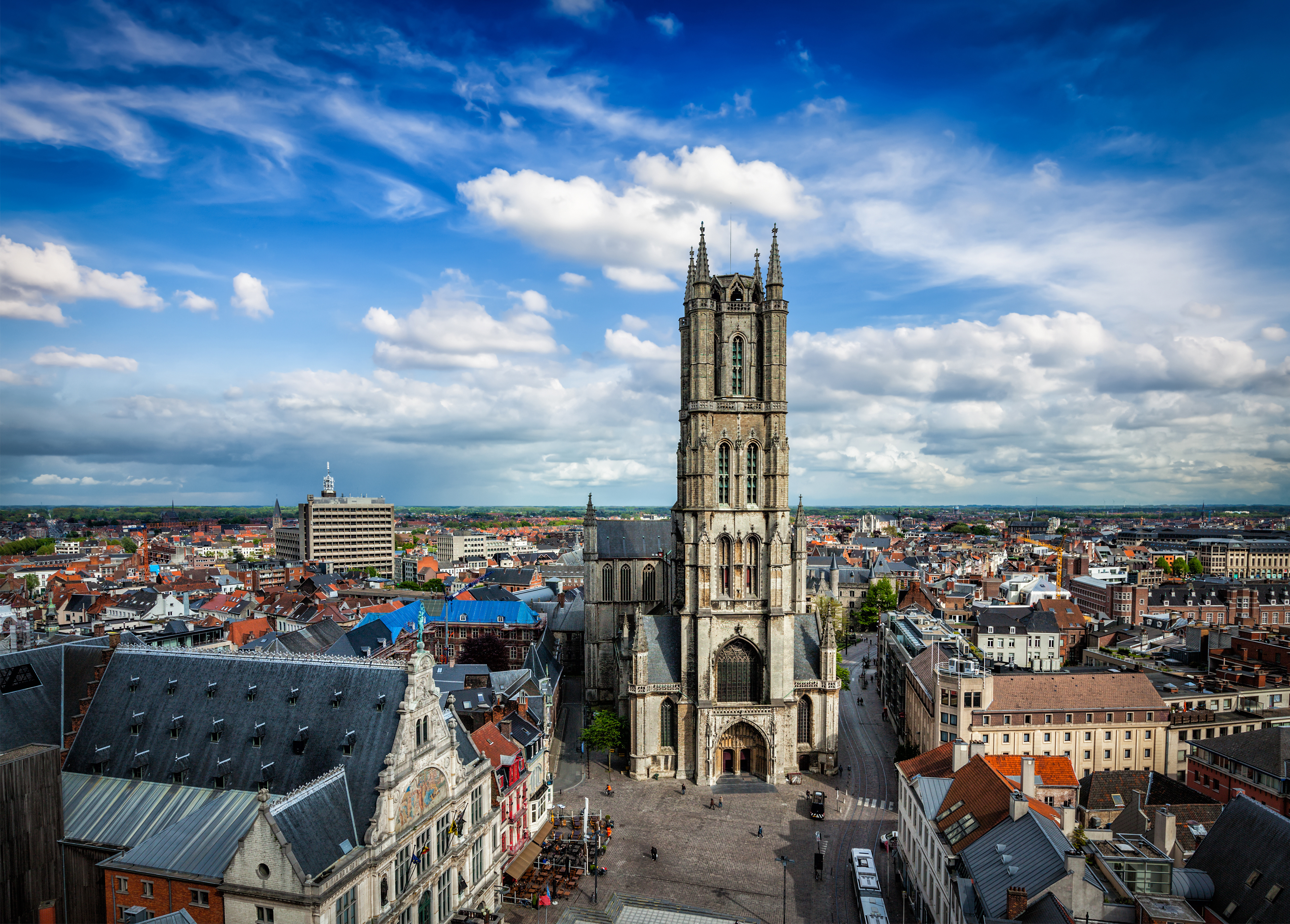 The impressive Saint Bavo's Cathedral, a tall gothic church located in the heart of Ghent, with a blue sky and white clouds in the background.