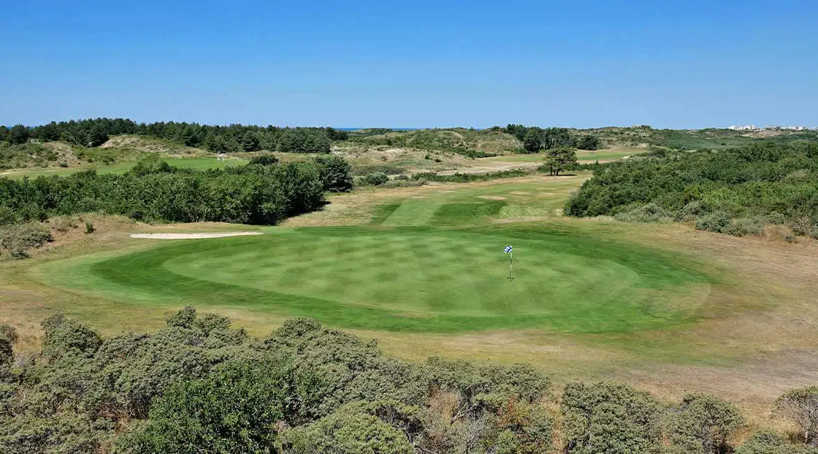 open golf course with surrounding greenery and blue sky