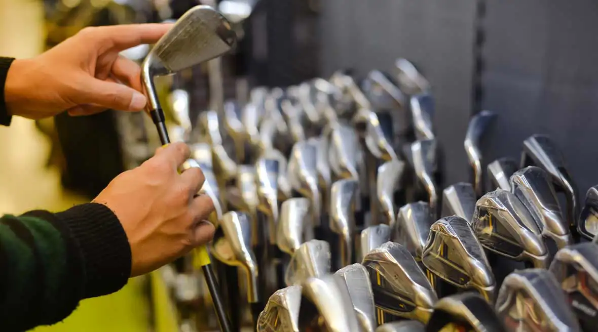 Person holding with hand golf club in a golf shop