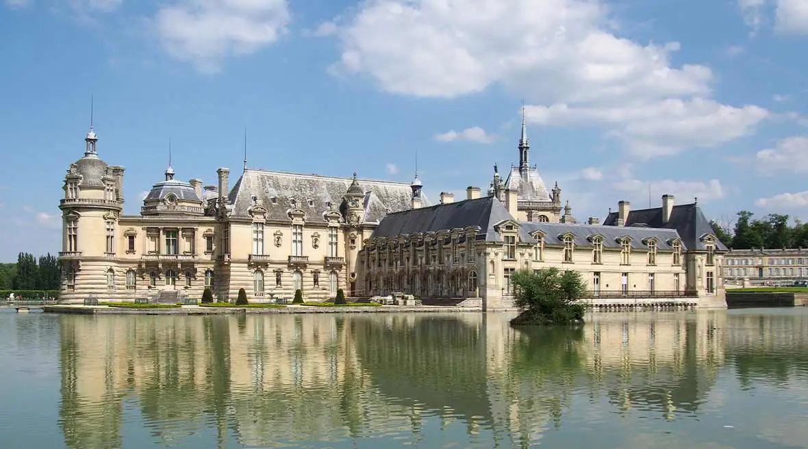 White brick French castle with turrets on a body of water under a blue sky
