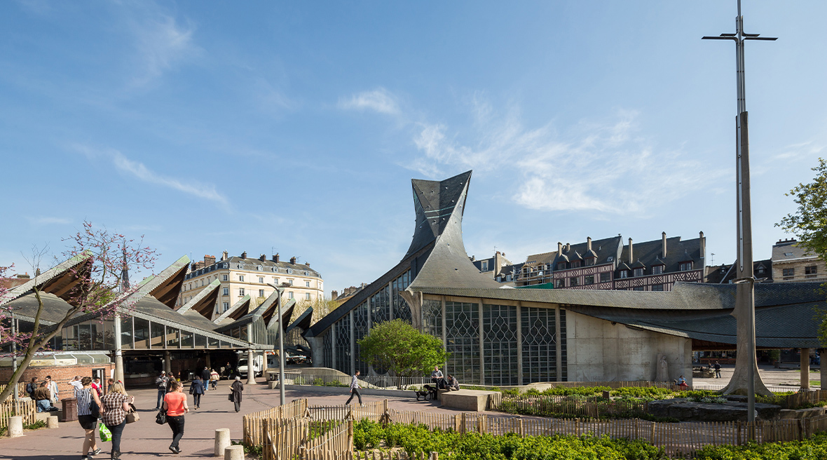 A modern church building with a distinctive roof and tall cross in a city square