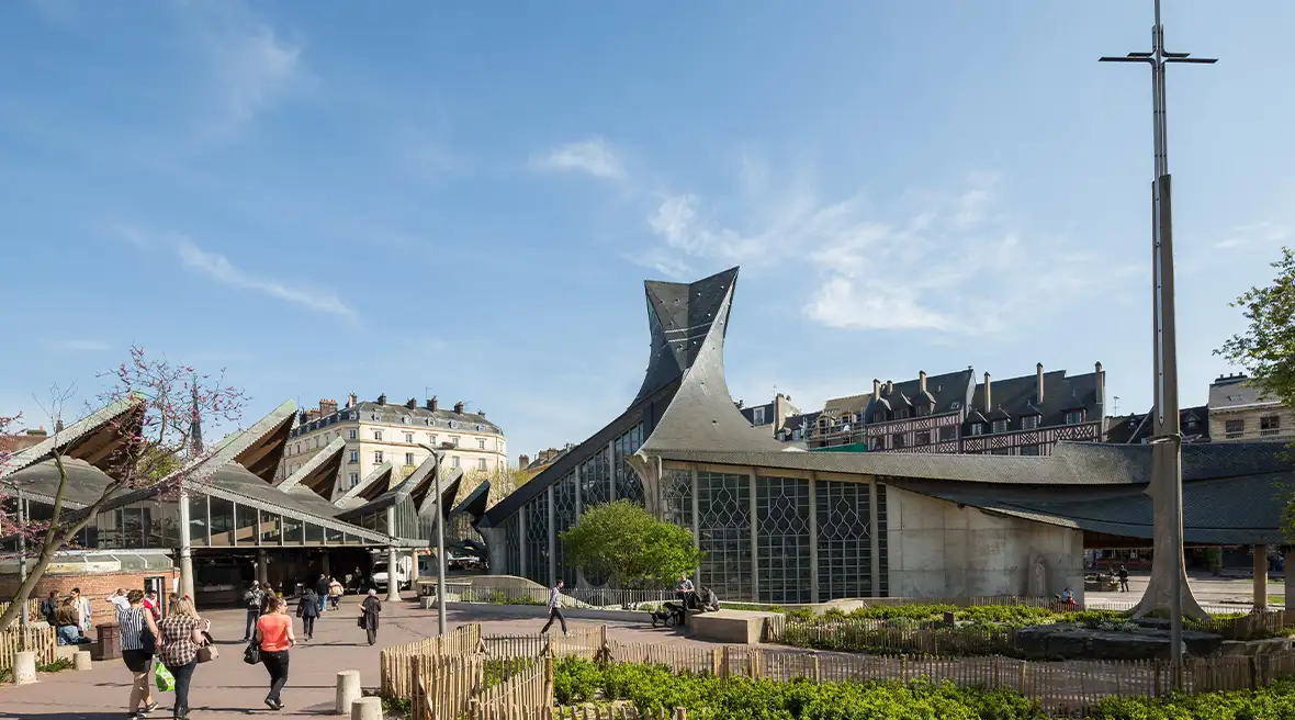 A modern church building with a distinctive roof and tall cross in a city square