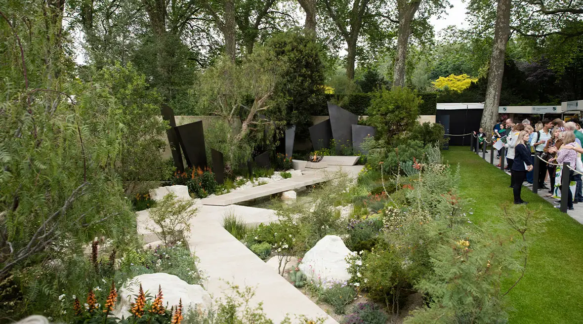 De ‘Telegraph Garden’ van de beroemde tuinarchitect Andy Sturgeon op de Chelsea Flower Show. Een moderne tuin met groene struiken en witte structuren. Bezoekers bekijken de tuin vanaf een afgezet pad.