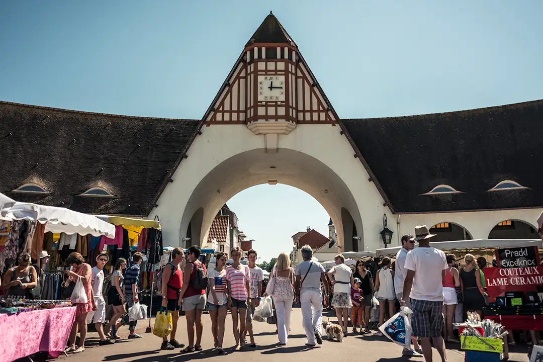 Les marchés à Le Touquet-Paris-Plage, a historic market under high arcades on a sunny day, full of people shopping.