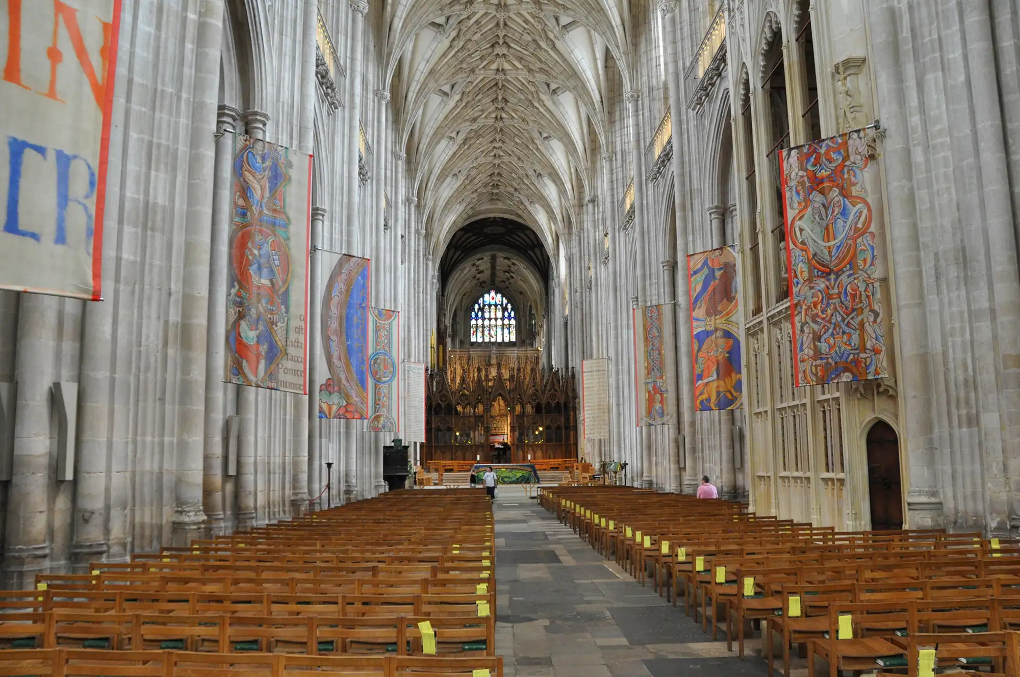 L’intérieur de la cathédrale de Winchester avec des bancs face à l’autel et des tapisseries suspendues aux piliers.
