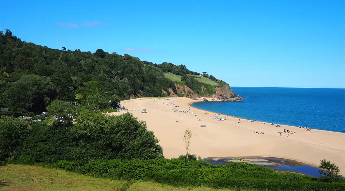 Quelques personnes sur la plage de sable doré de Blackpool Sands entre des falaises verdoyantes et l’eau limpide de la mer
