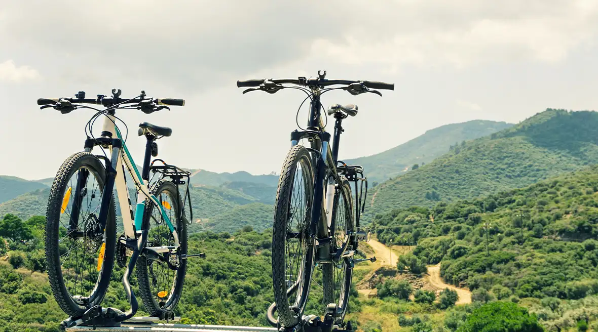 Two mountain bikes attached to the roof of a vehicle you can’t see with green mountains in the distance