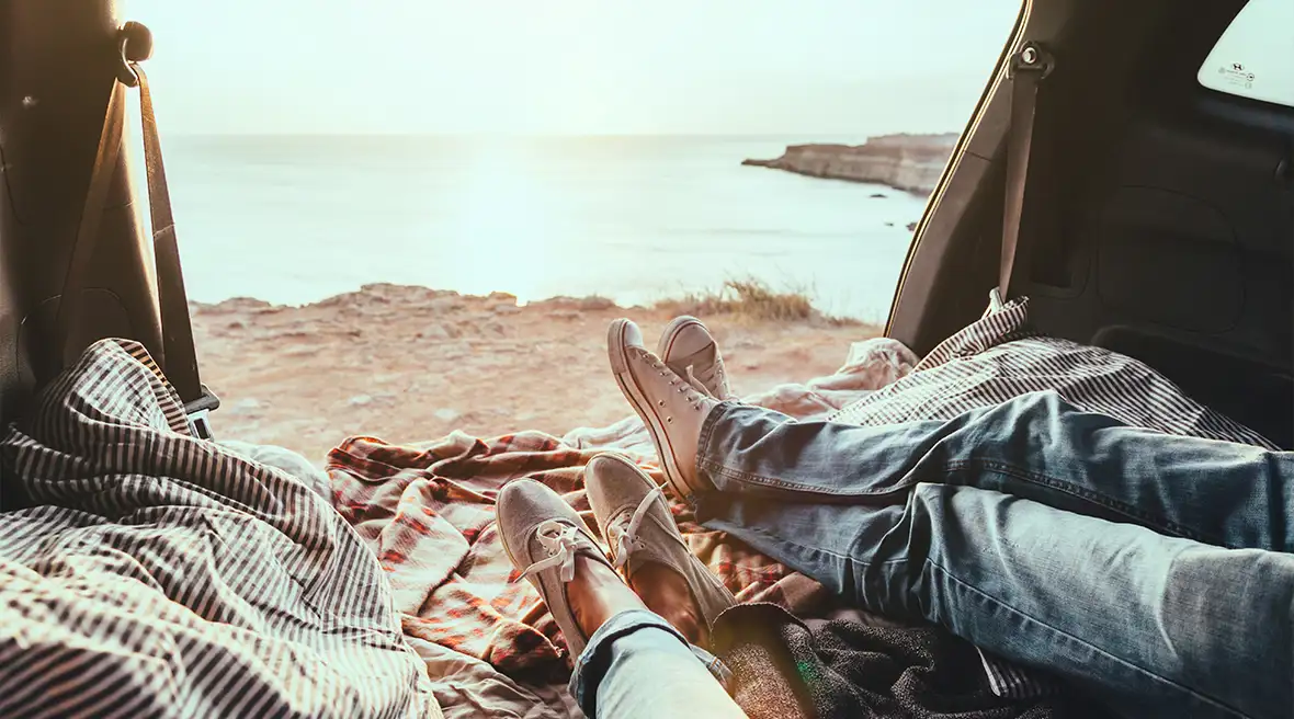 Two pairs of legs in casual clothing stretched out on blankets and relaxing on a beach