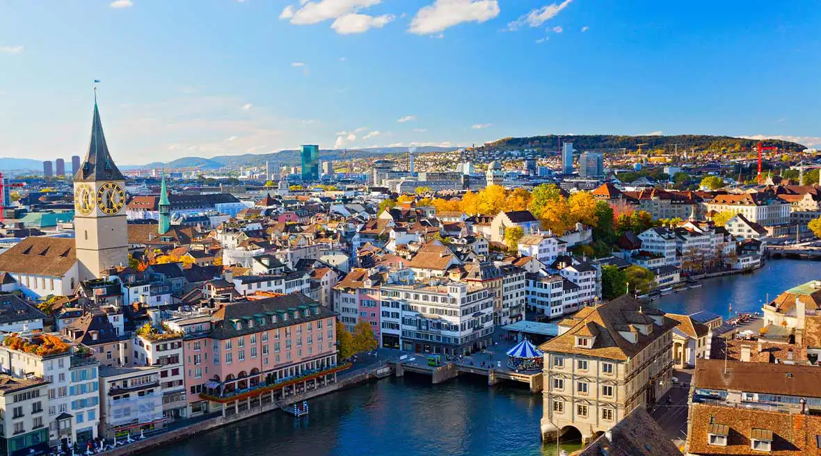panoramic view of a city set on a river with colourful buildings and a large clock tower