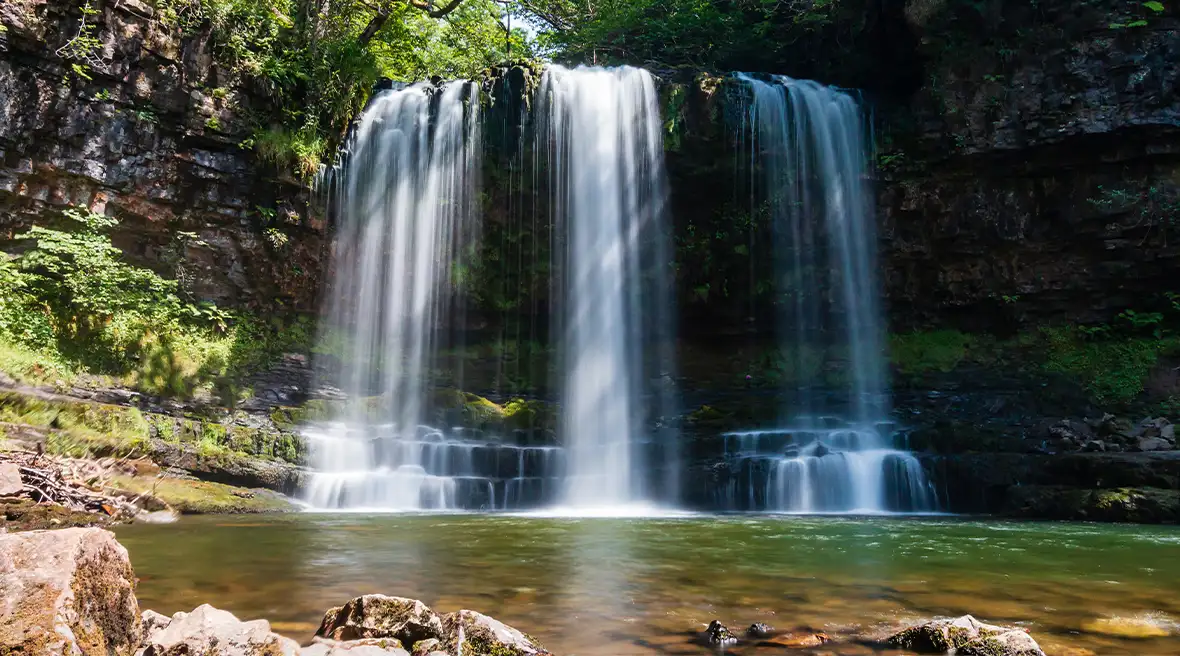 Cascade se jetant dans un plan d’eau verte, entouré d’arbres, de verdure et de roches grises