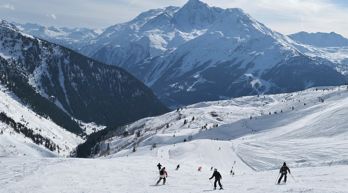 Skiers skiing down a slope looking down towards a spectacular Alpine valley
