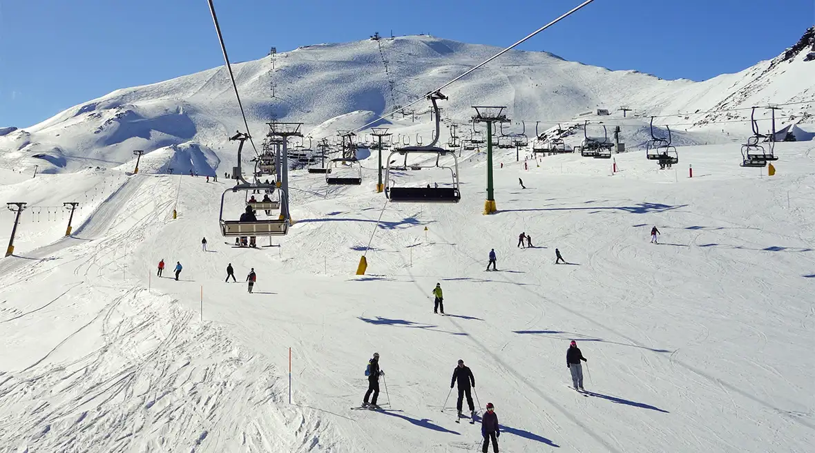 People skiing down the mountain in La Rosière beneath other skiers using ski lifts to go back up the mountain