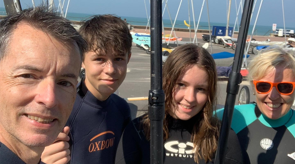 A family of four wearing wetsuits and holding paddles on the beach front in Le Touquet