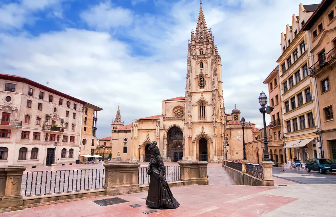 Impressive cathedral against a blue sky set in a Spanish town square with a bronze statue of a woman in the foreground