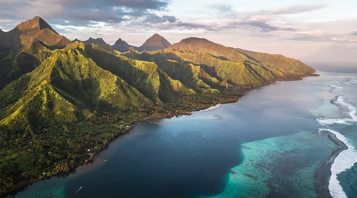 Waves rolling into a mountainous island at sunset 