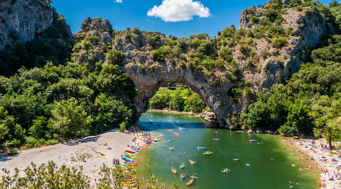 blue green waters with people swimming with a huge stone archway above it