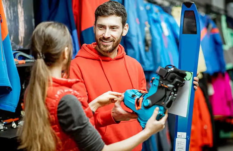 Man and woman choosing sports equipment looking on the ski and boots for skiing in the shop