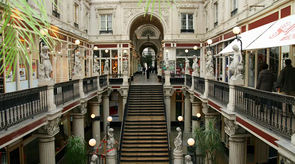 Ornate stairway leading to a passage of shops under a glass ceiling