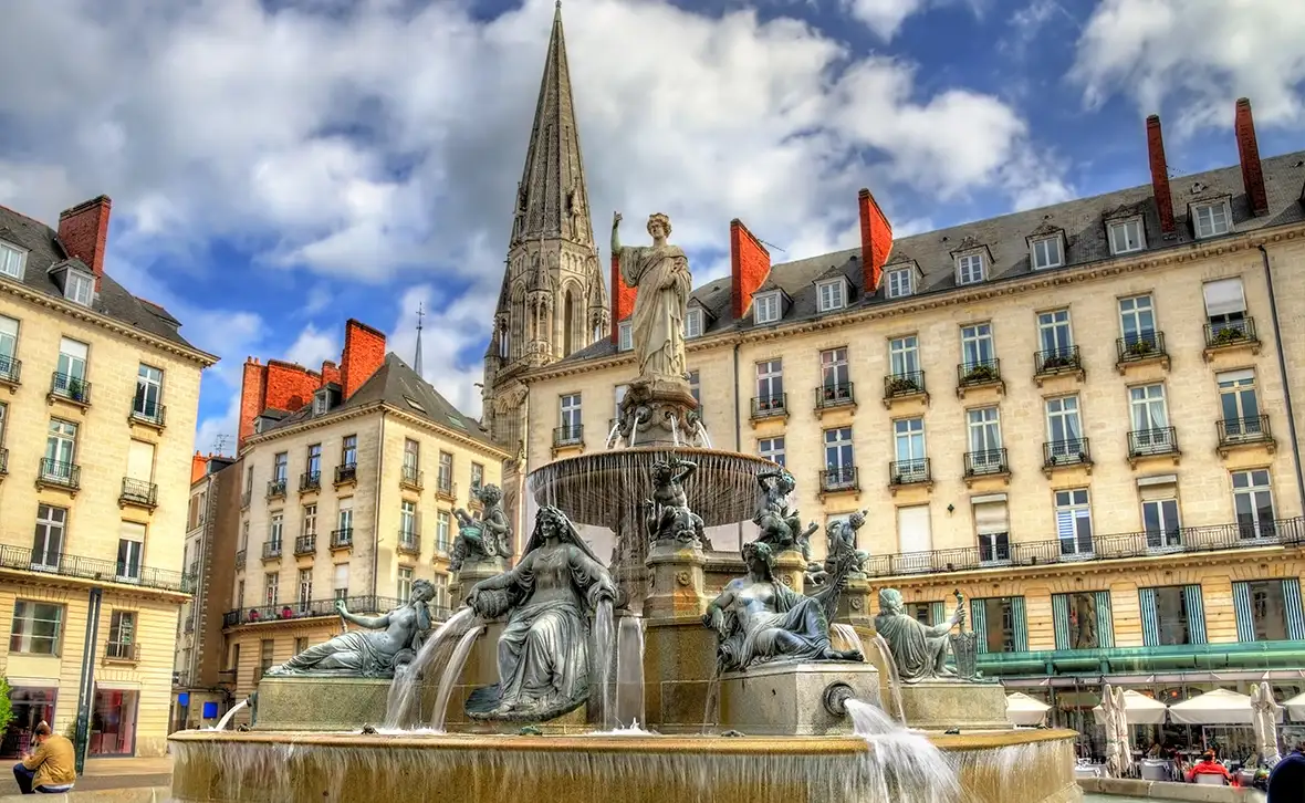 multi-tiered fountain with many figures seated and standing with water spouting from them in front of a large building under a blue sky
