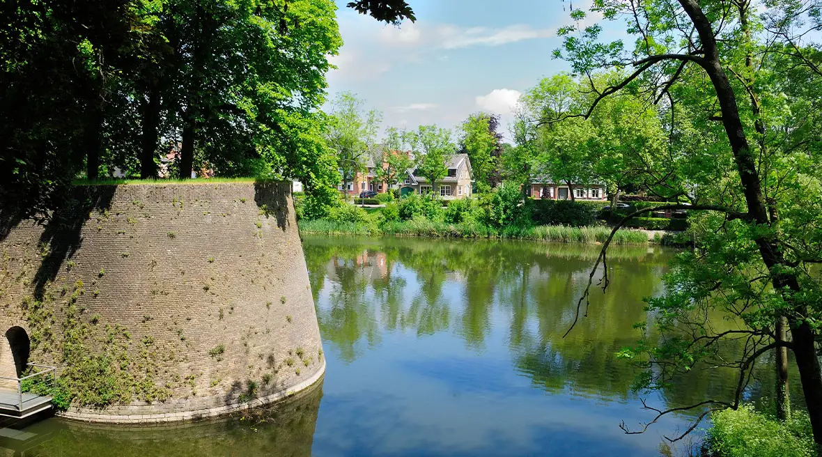 View of a waterway with a rampart or fortification in the foreground and houses on the far bank