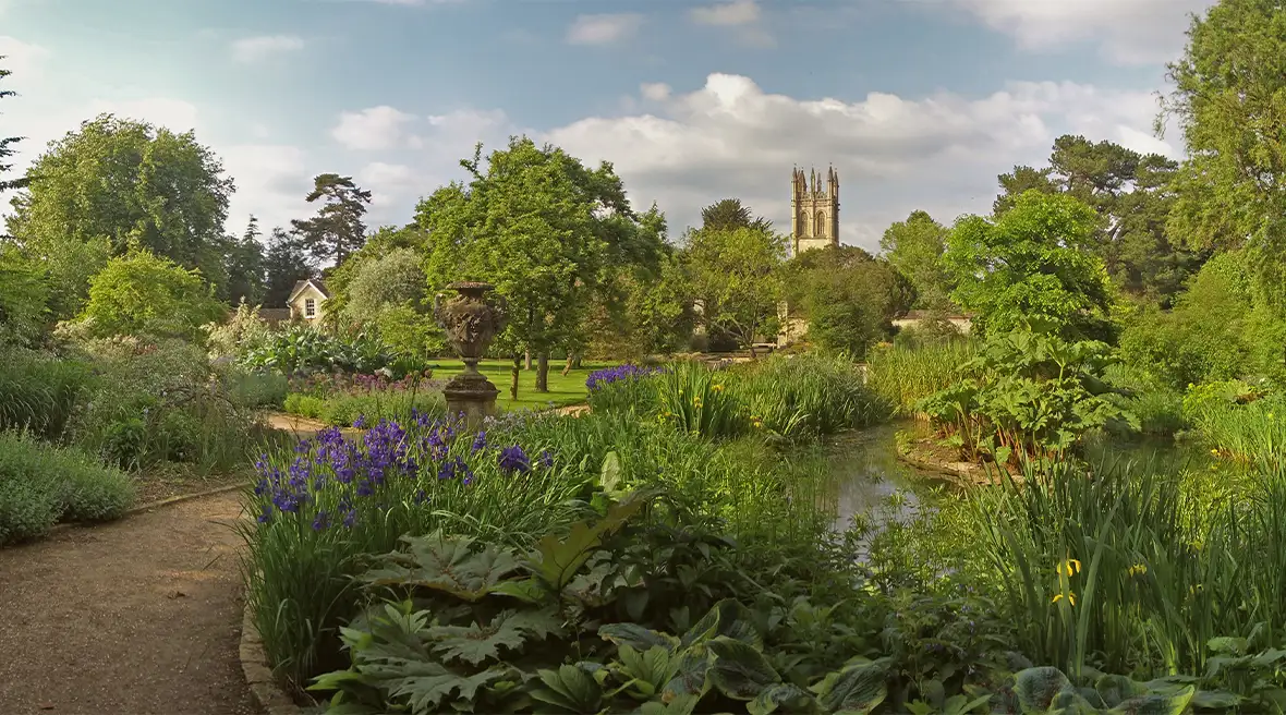 Tuinpad langs vijver met op de voorgrond bloemen, op de achtergrond een middeleeuwse toren