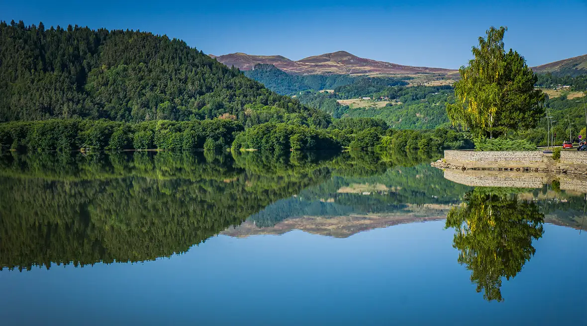 lake reflecting blue skies and trees with a small jetty stretching into the blue water